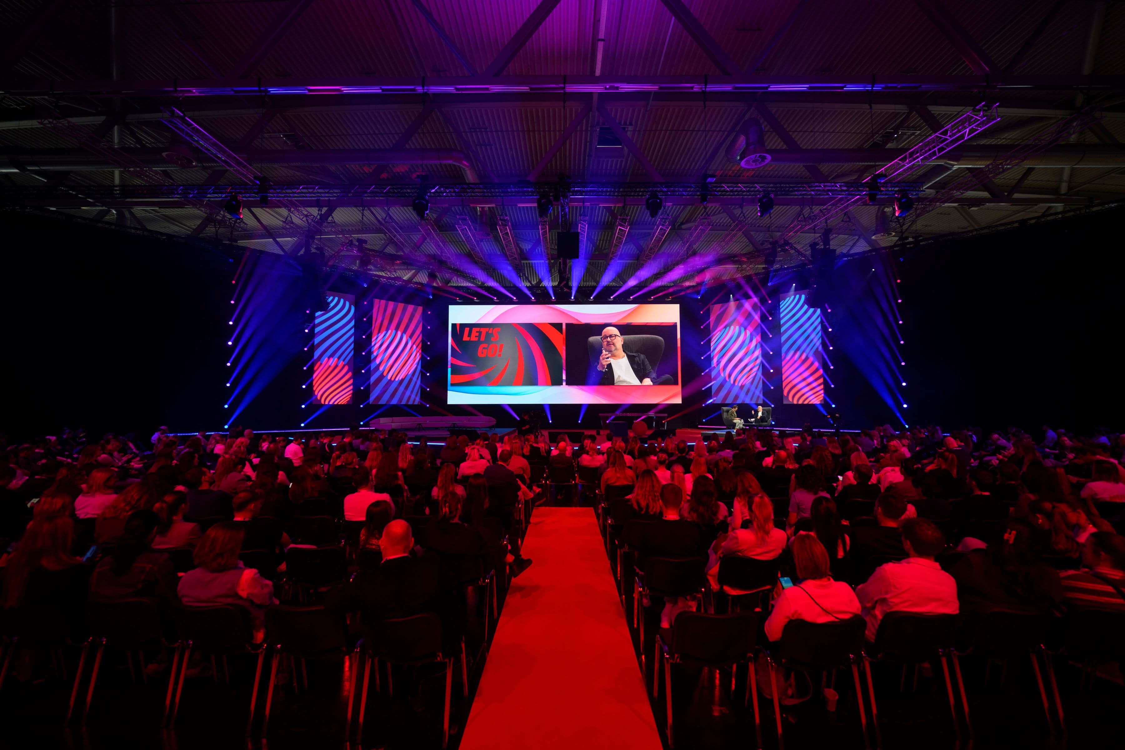 Große DMEXCO-Bühne mit farbiger Lichtshow vor dicht besetztem Publikum in einer Messehalle.