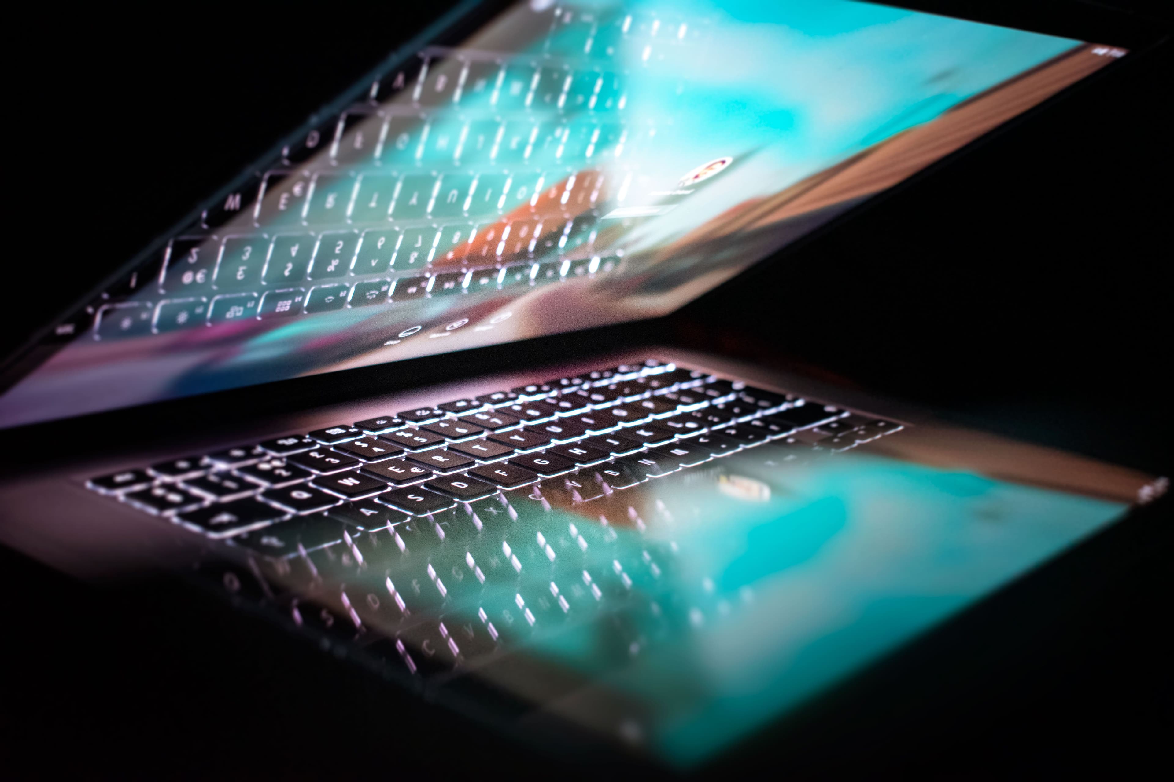 Ein Laptop spiegelt sich in einer dunklen Oberfläche mit farbigem Licht.