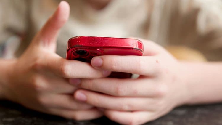 Junge Person hält ein Smartphone als Symbol für Altersprüfung und Jugendschutz im Netz