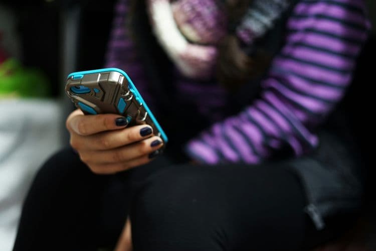 Jugendliche Person nutzt ein Smartphone in einer dunkleren Umgebung.