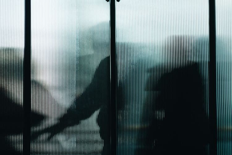 Verschwommene Silhouetten von Menschen hinter einer geriffelten Glasfläche.