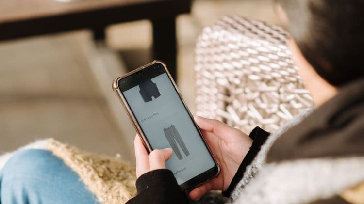 Eine Person nutzt ein Smartphone zum Online-Shopping und sieht sich Kleidung in einer App an.