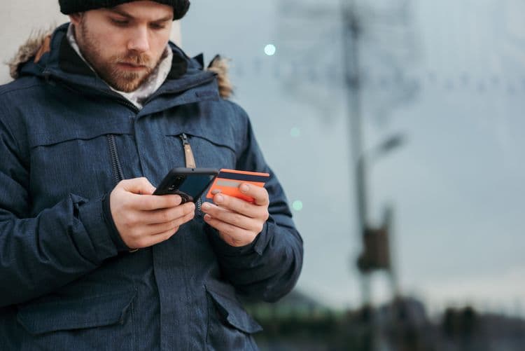 Eine Person nutzt ein Smartphone und hält eine Zahlungskarte in der Hand.