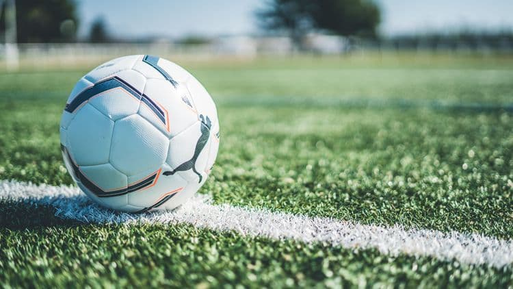 Ein weißer Fußball liegt auf einem Fußballfeld an der Seitenlinie, der Hintergrund ist unscharf.