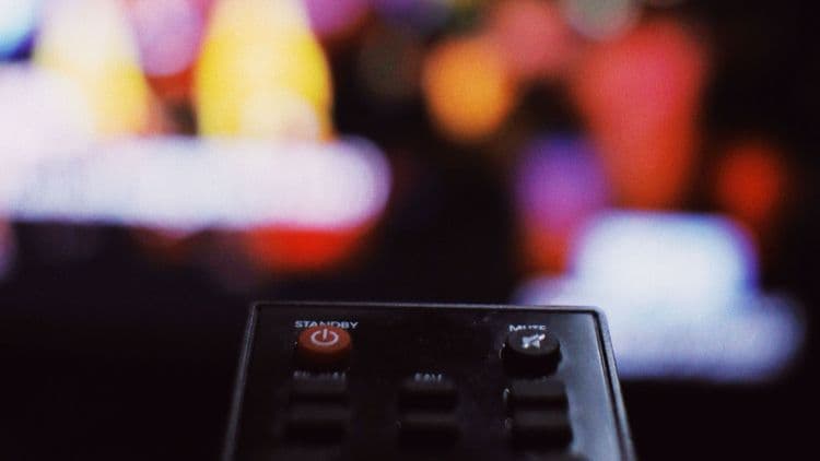 Fernbedienung vor einem unscharfen TV-Bildschirm mit Streaming-Oberfläche