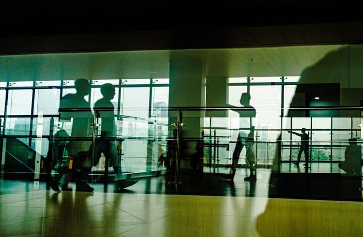 Silhouetten und Spiegelungen mehrerer Menschen hinter einer Glasfassade.
