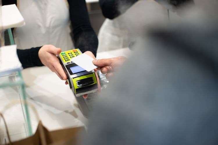 Eine Person bezahlt an einer Ladenkasse mit einer Karte an einem Kartenterminal.