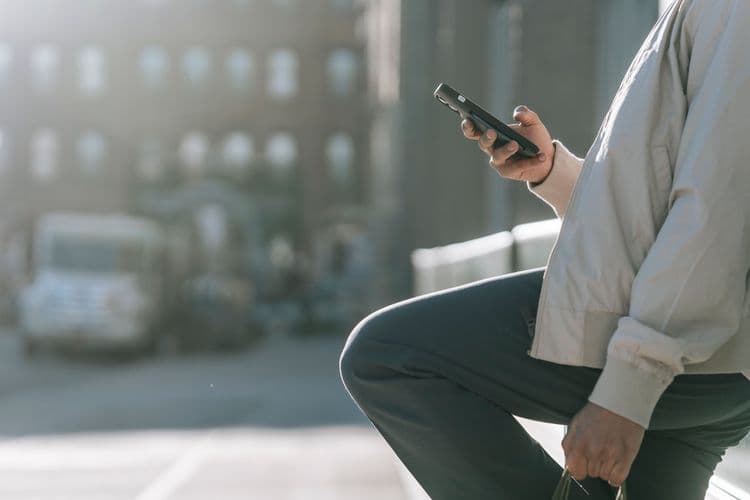 Eine Person nutzt unterwegs ein Smartphone vor unscharfem städtischem Hintergrund.