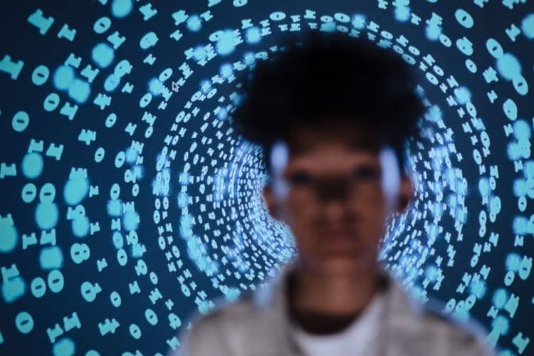 Unscharfe Person vor einer digitalen Oberfläche aus Nullen und Einsen.
