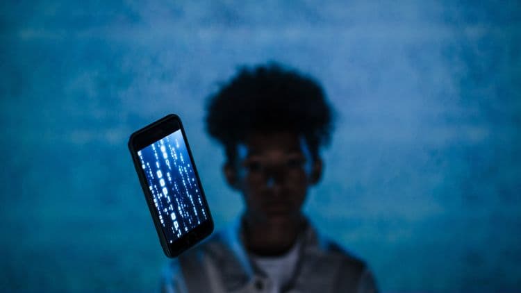 Smartphone mit leuchtendem Code vor einer unscharfen Person