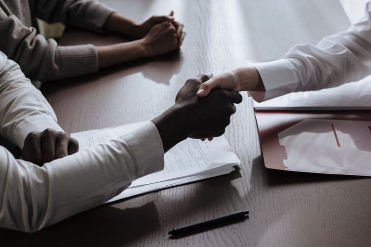 Zwei Personen reichen sich über einem Tisch mit Unterlagen die Hand.