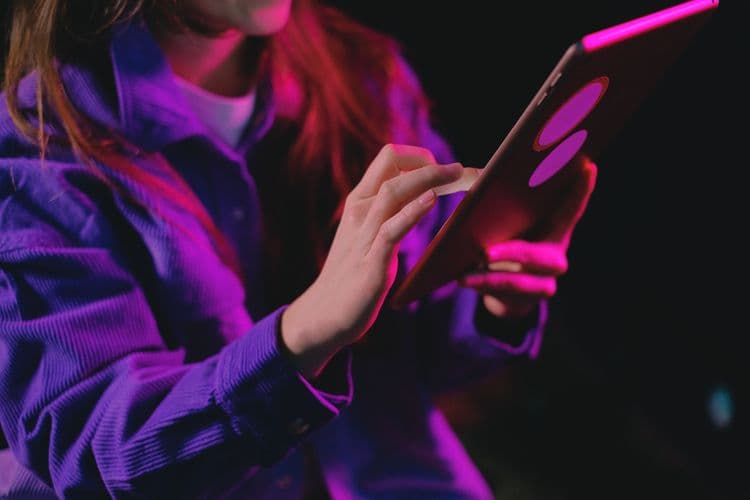 Eine Person nutzt ein Tablet in farbigem Licht.