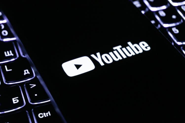 YouTube-Logo auf einem Smartphone-Display neben einer beleuchteten Tastatur.