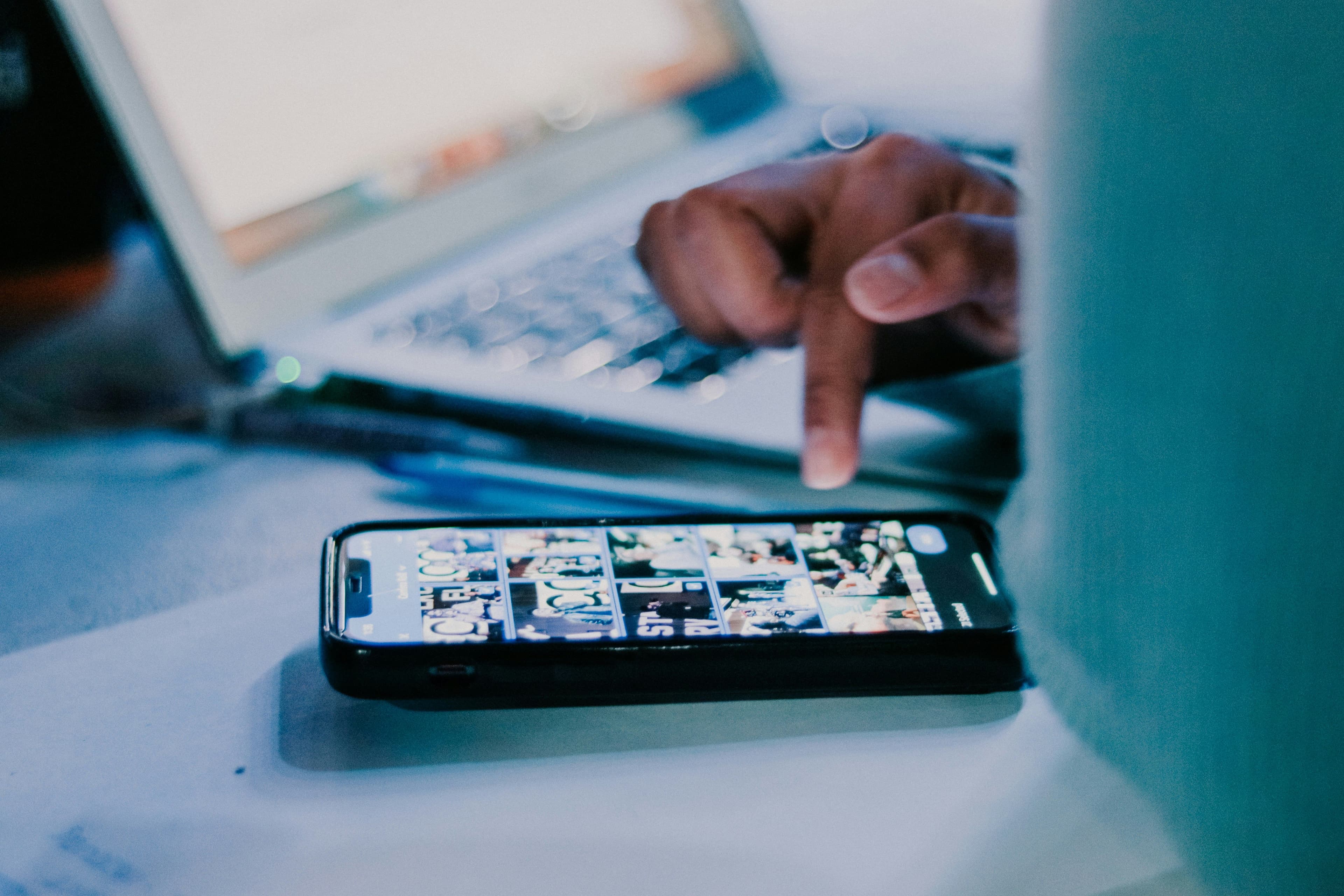 Eine Person scrollt auf einem Smartphone durch einen bildbasierten Feed, im Hintergrund ist ein Laptop zu sehen.