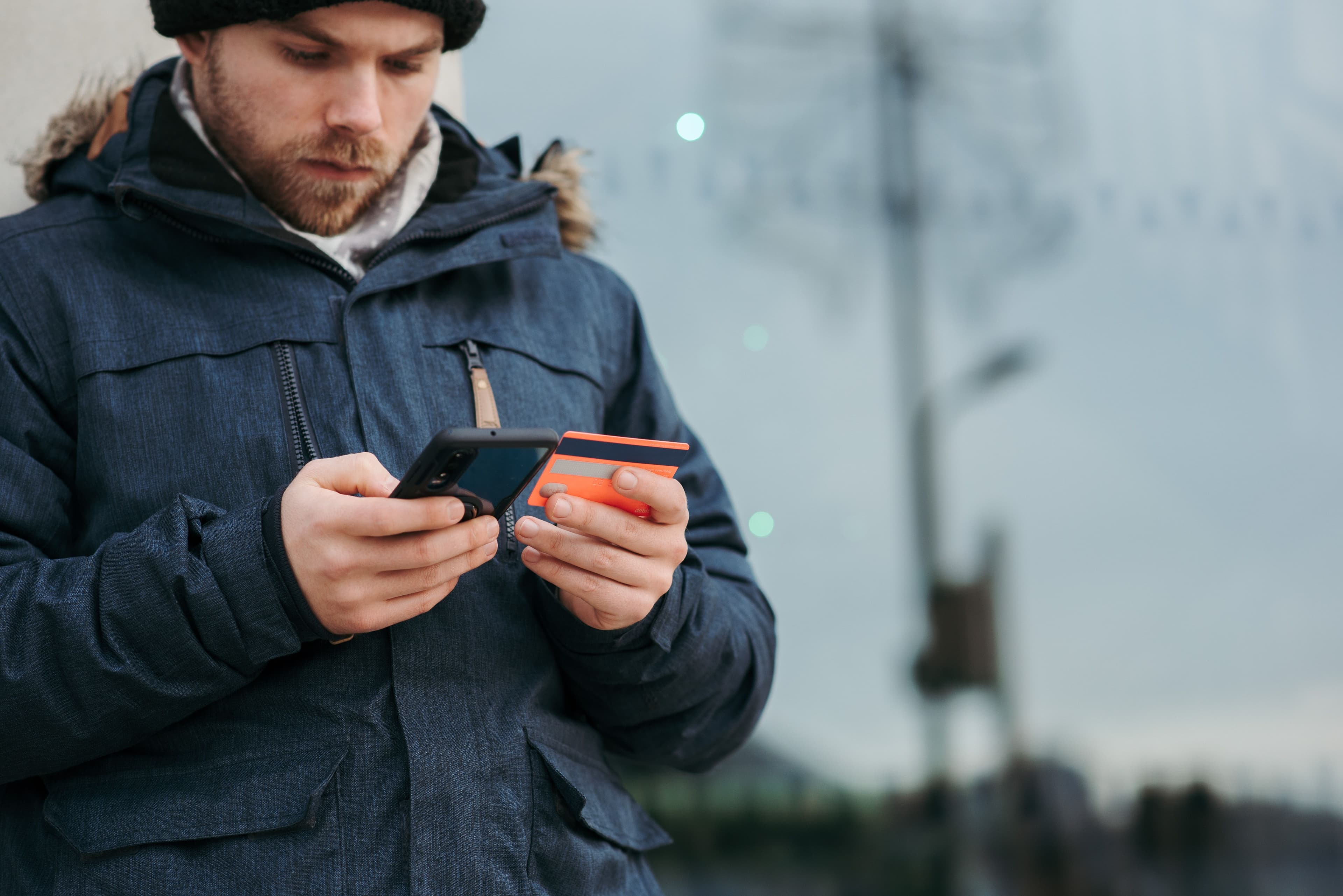 Eine Person nutzt ein Smartphone und hält eine Zahlungskarte in der Hand.