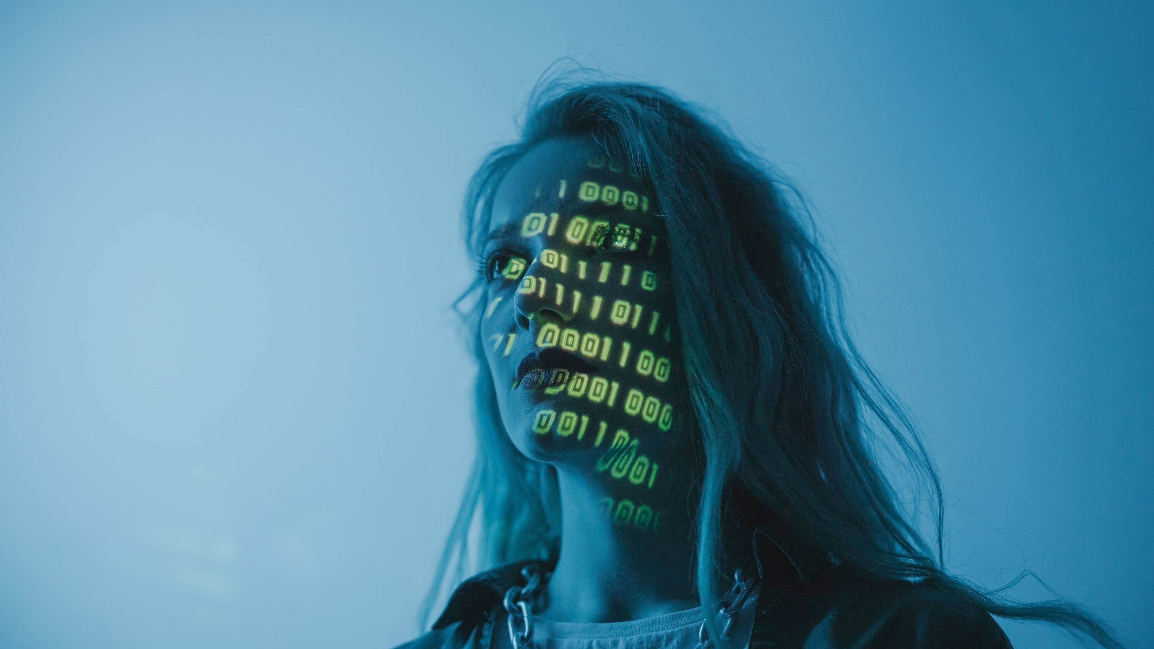 Woman with binary code projected onto her face against a blue background.