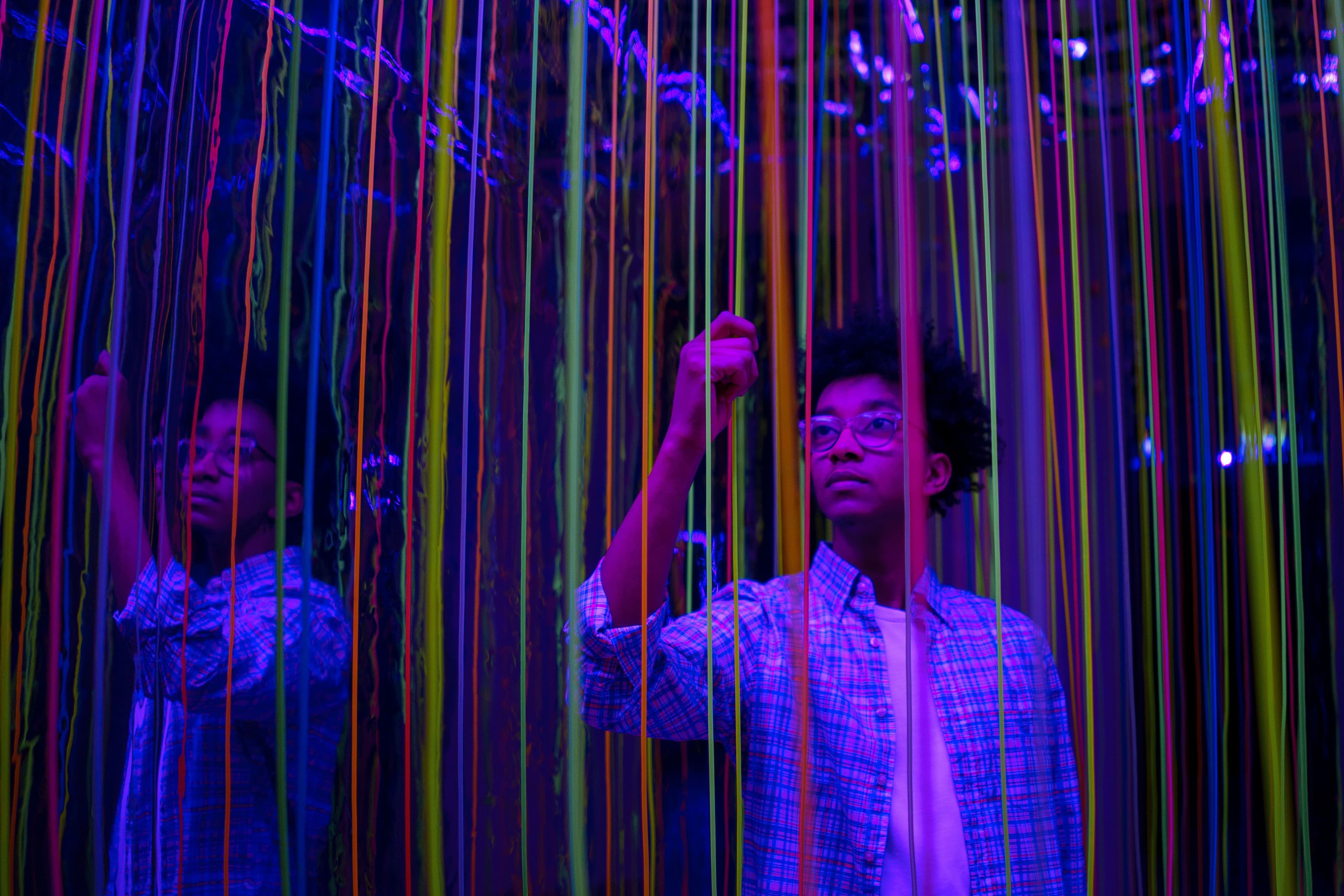 Person zwischen farbigen vertikalen Lichtlinien und Spiegelungen in einer digitalen Installation.