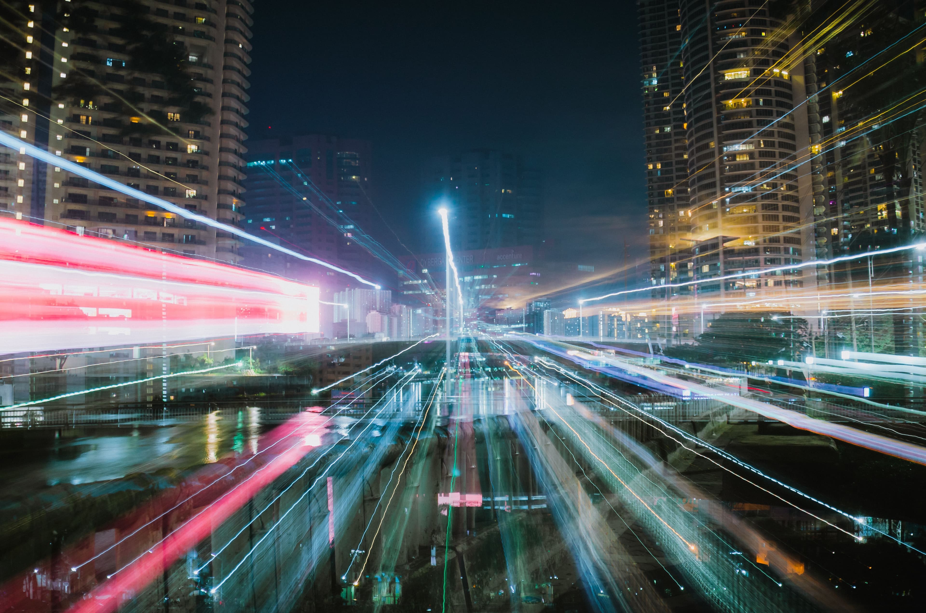Nächtliche Stadtansicht mit Lichtspuren zwischen Hochhäusern, die Bewegung und Datenströme im urbanen Raum symbolisieren.