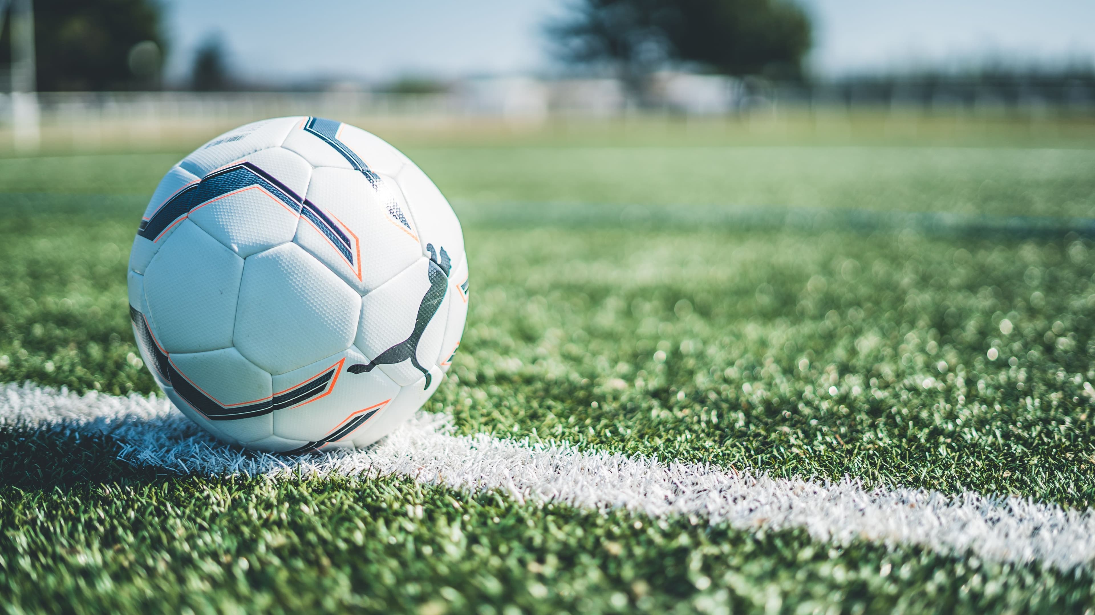 Ein weißer Fußball liegt auf einem Fußballfeld an der Seitenlinie, der Hintergrund ist unscharf.