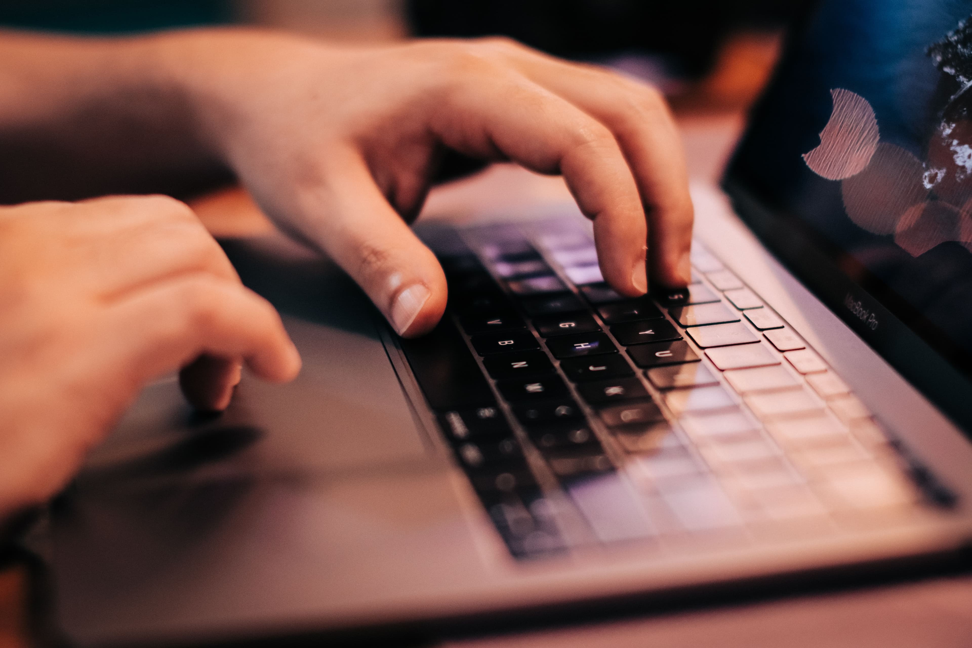 Hände tippen auf einer Laptop-Tastatur, der Bildschirm ist nur angeschnitten und unscharf zu sehen.