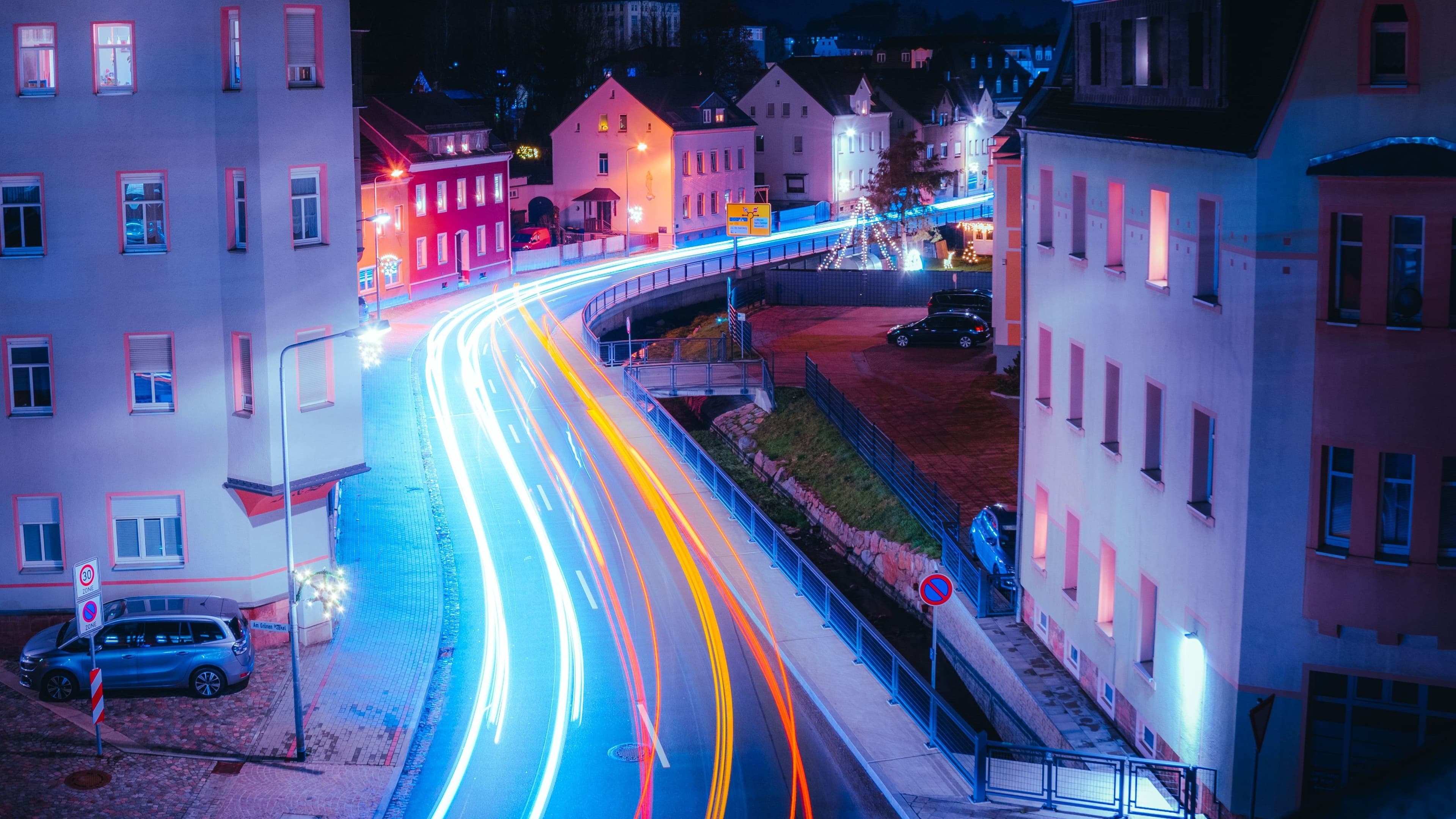 Nächtliche Straße mit hellen Lichtspuren zwischen Wohnhäusern.