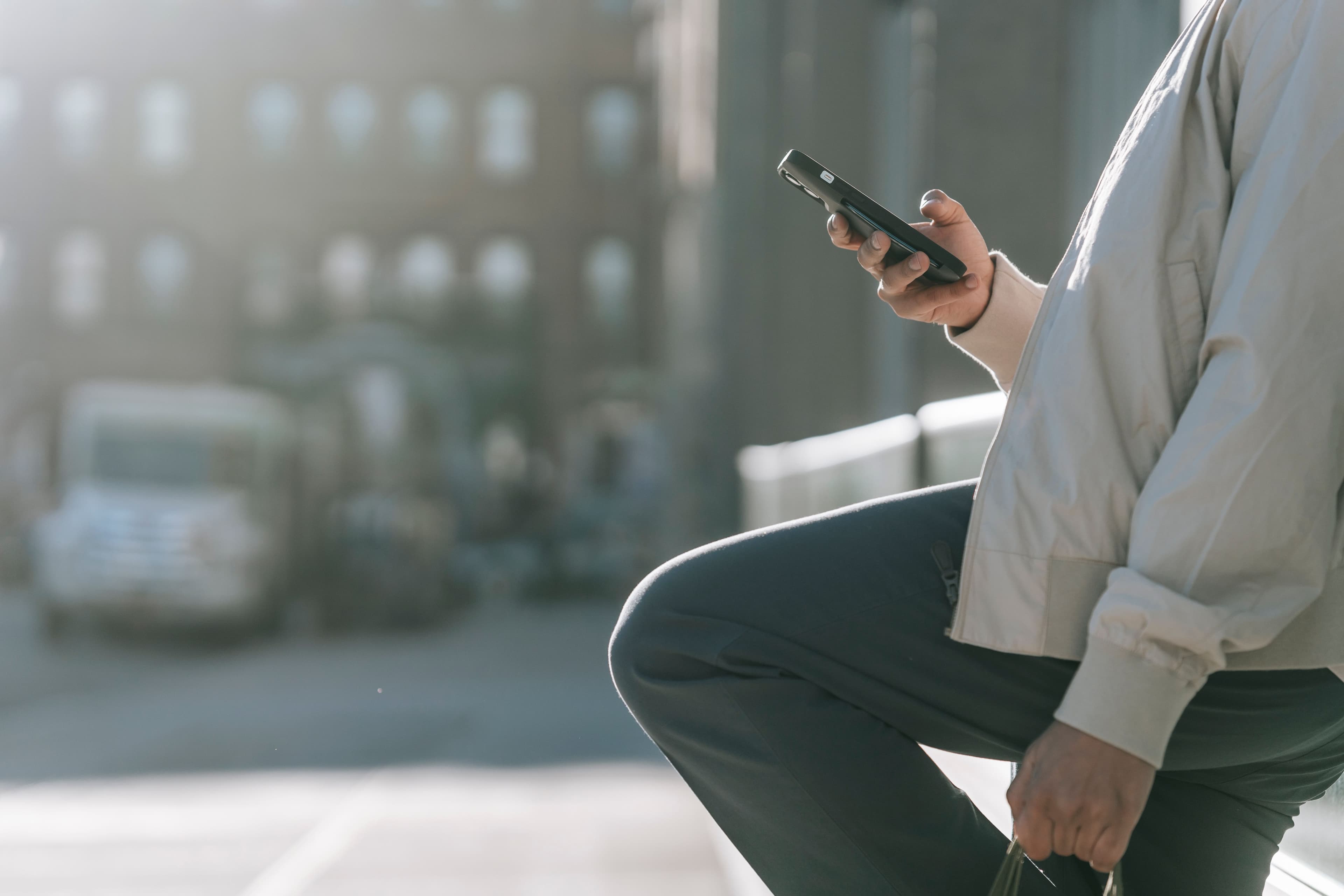 Eine Person nutzt unterwegs ein Smartphone vor unscharfem städtischem Hintergrund.