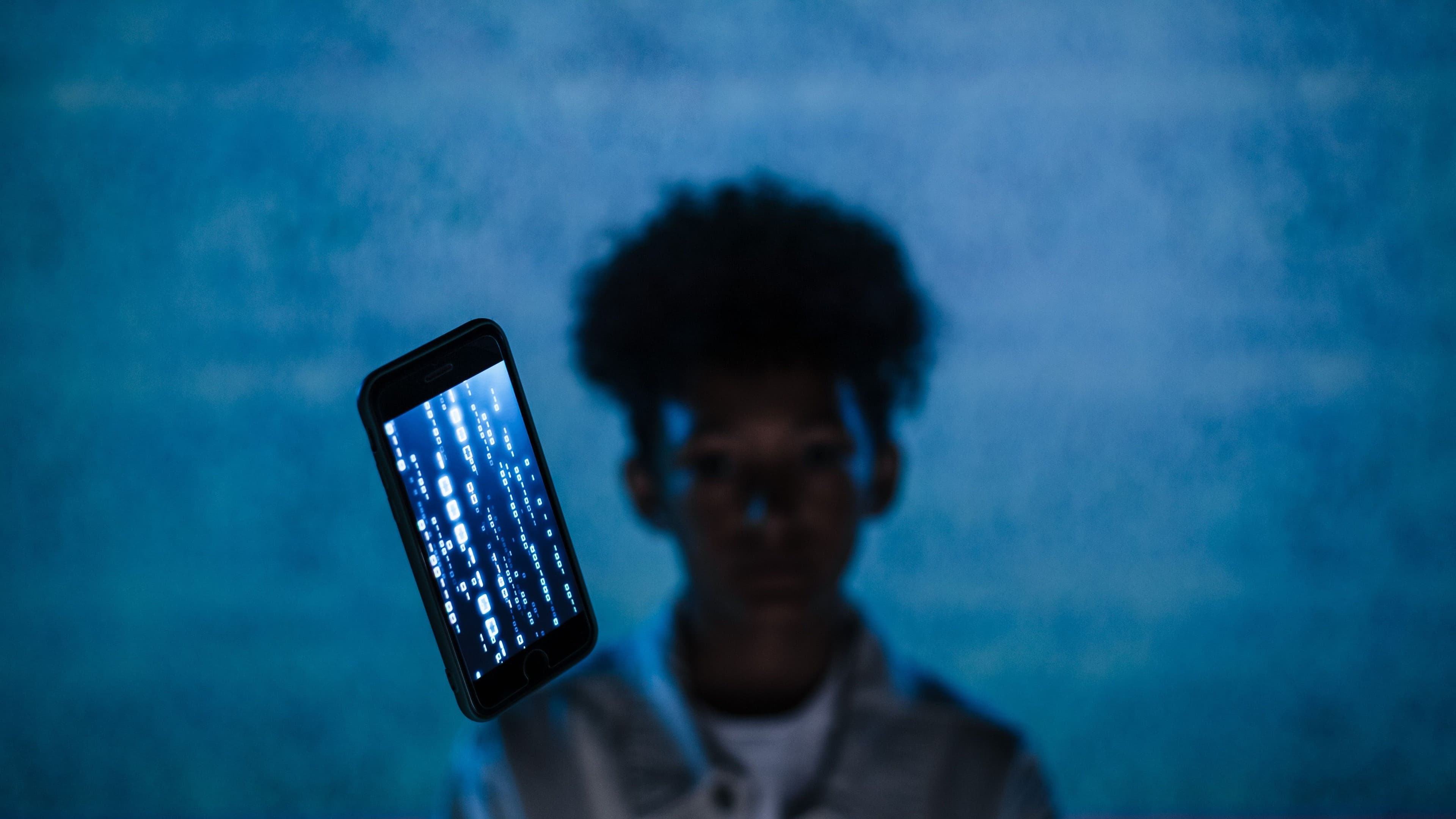 Smartphone mit leuchtendem Code vor einer unscharfen Person