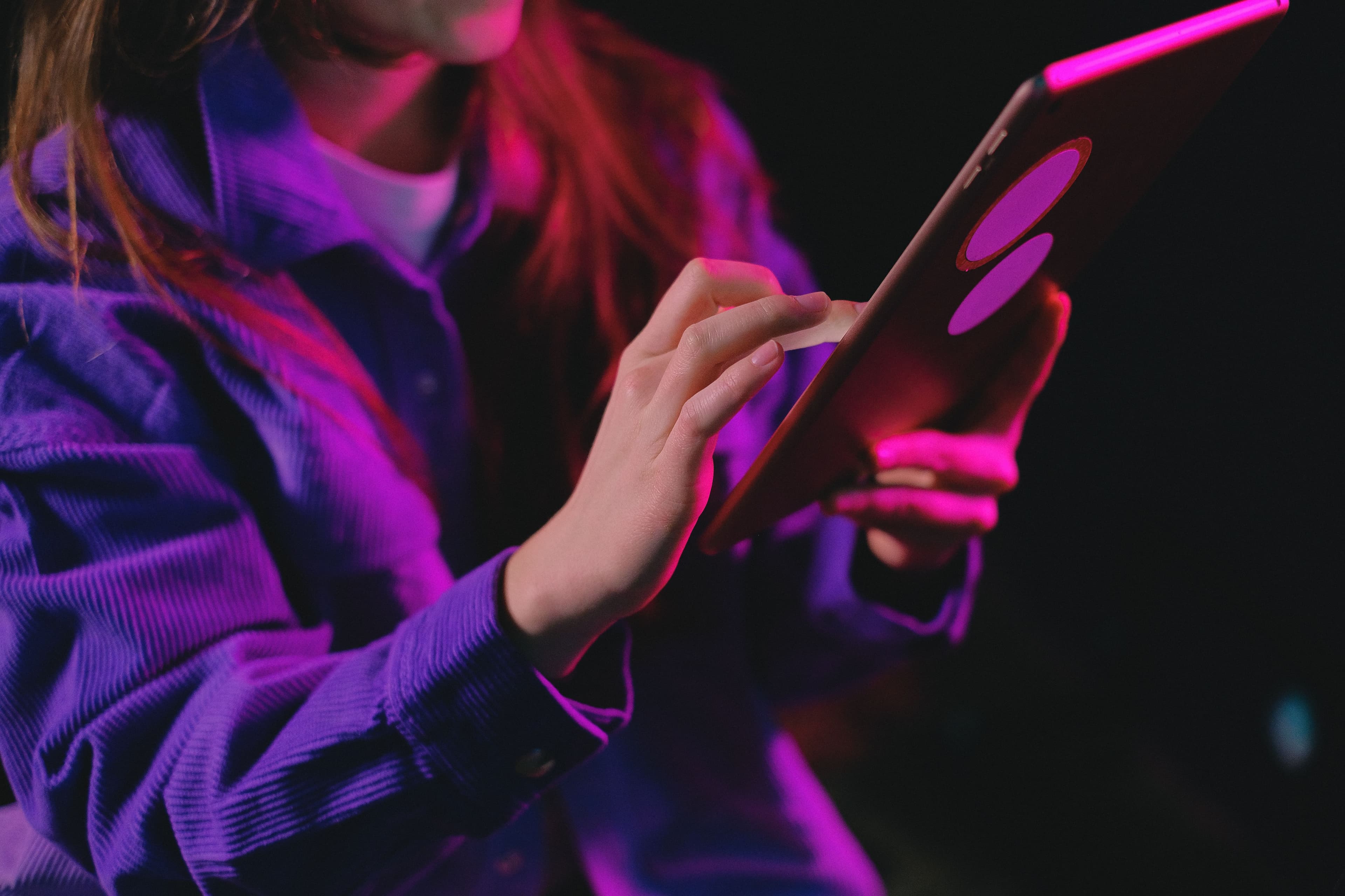 Eine Person nutzt ein Tablet in farbigem Licht.