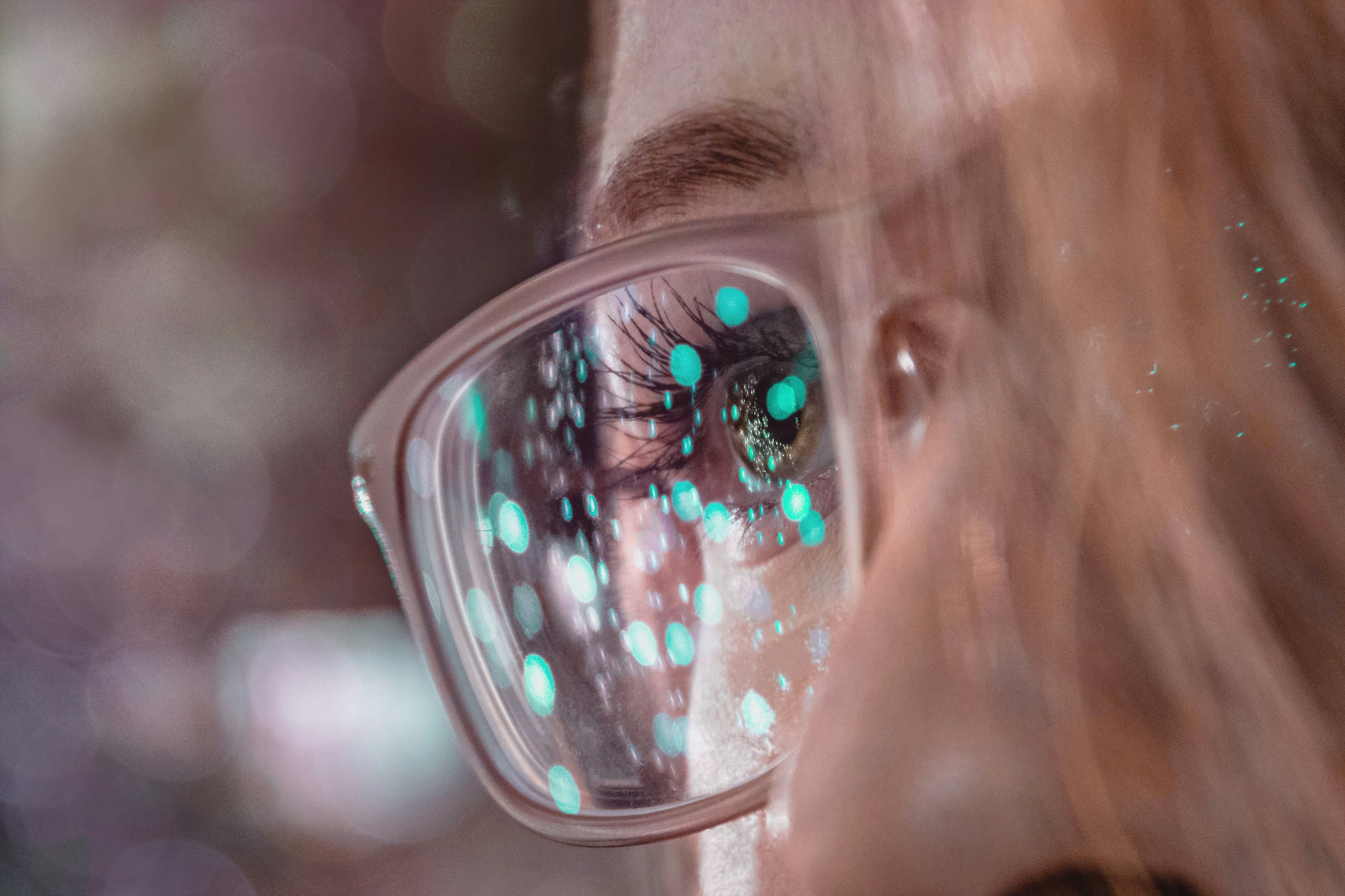 Nahaufnahme einer Person mit Brille, in deren Glas sich digitale Lichtpunkte spiegeln.