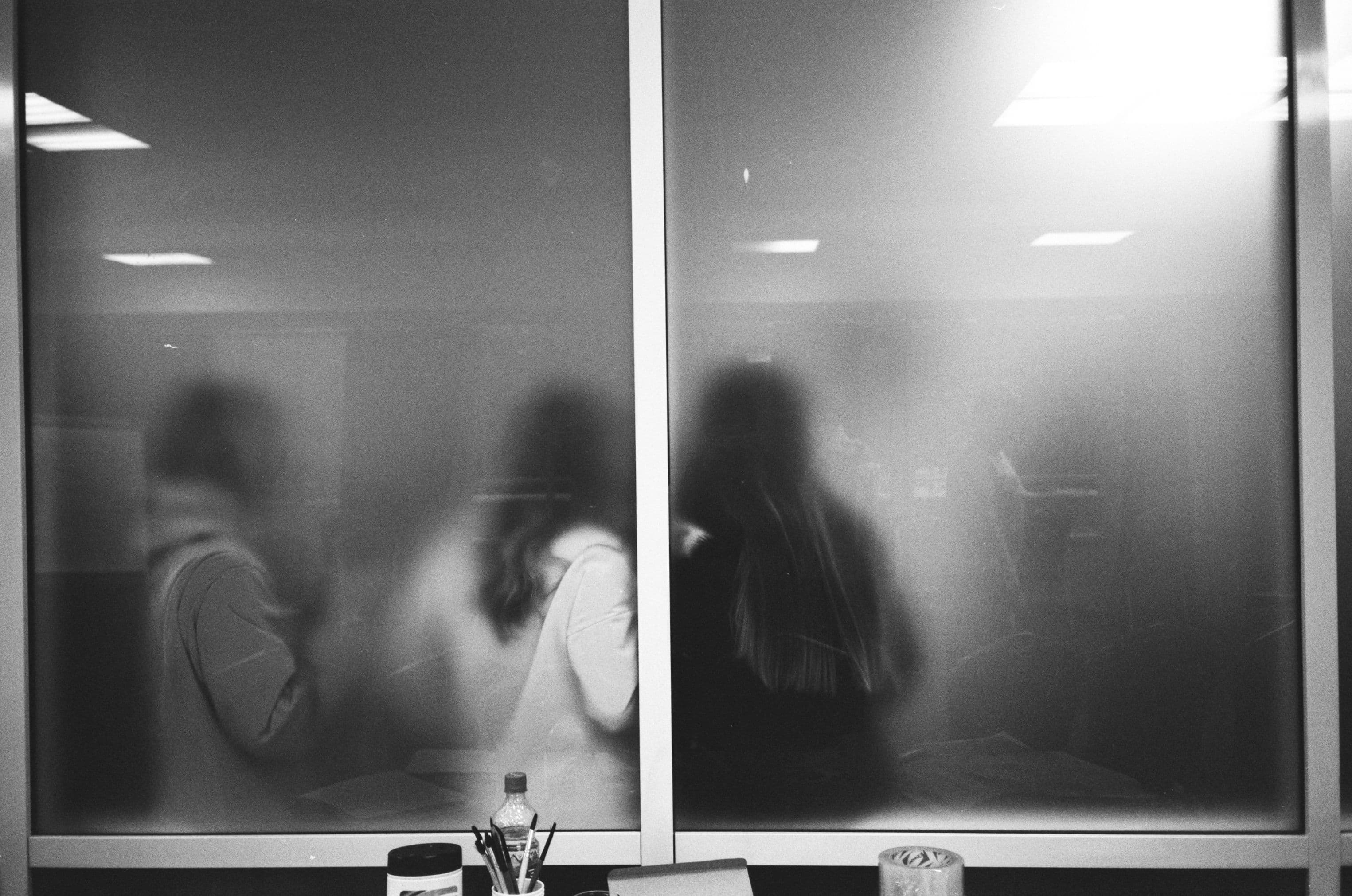 Unscharfe Personen hinter einer Glasscheibe in einem Büro.