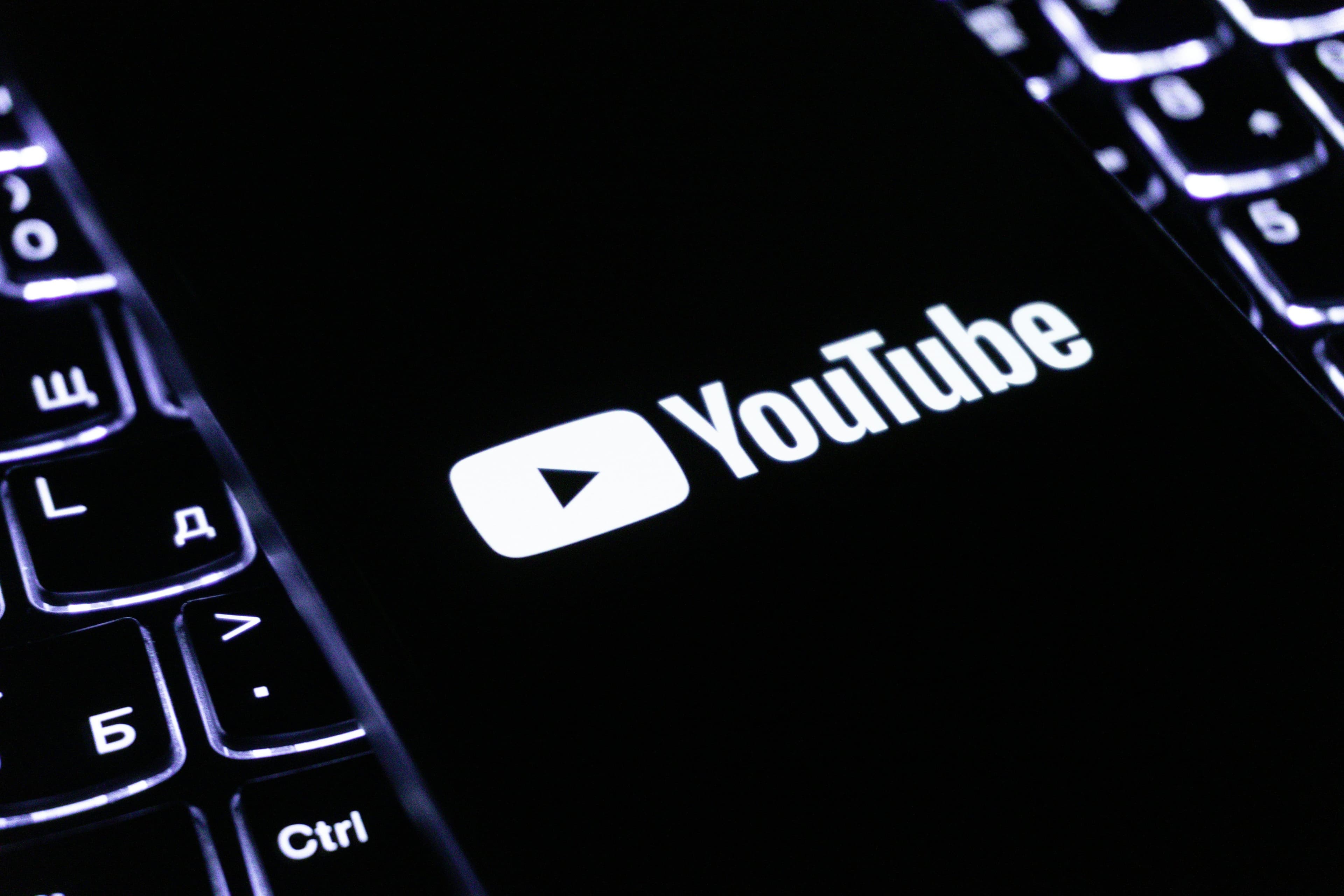 YouTube-Logo auf einem Smartphone-Display neben einer beleuchteten Tastatur.