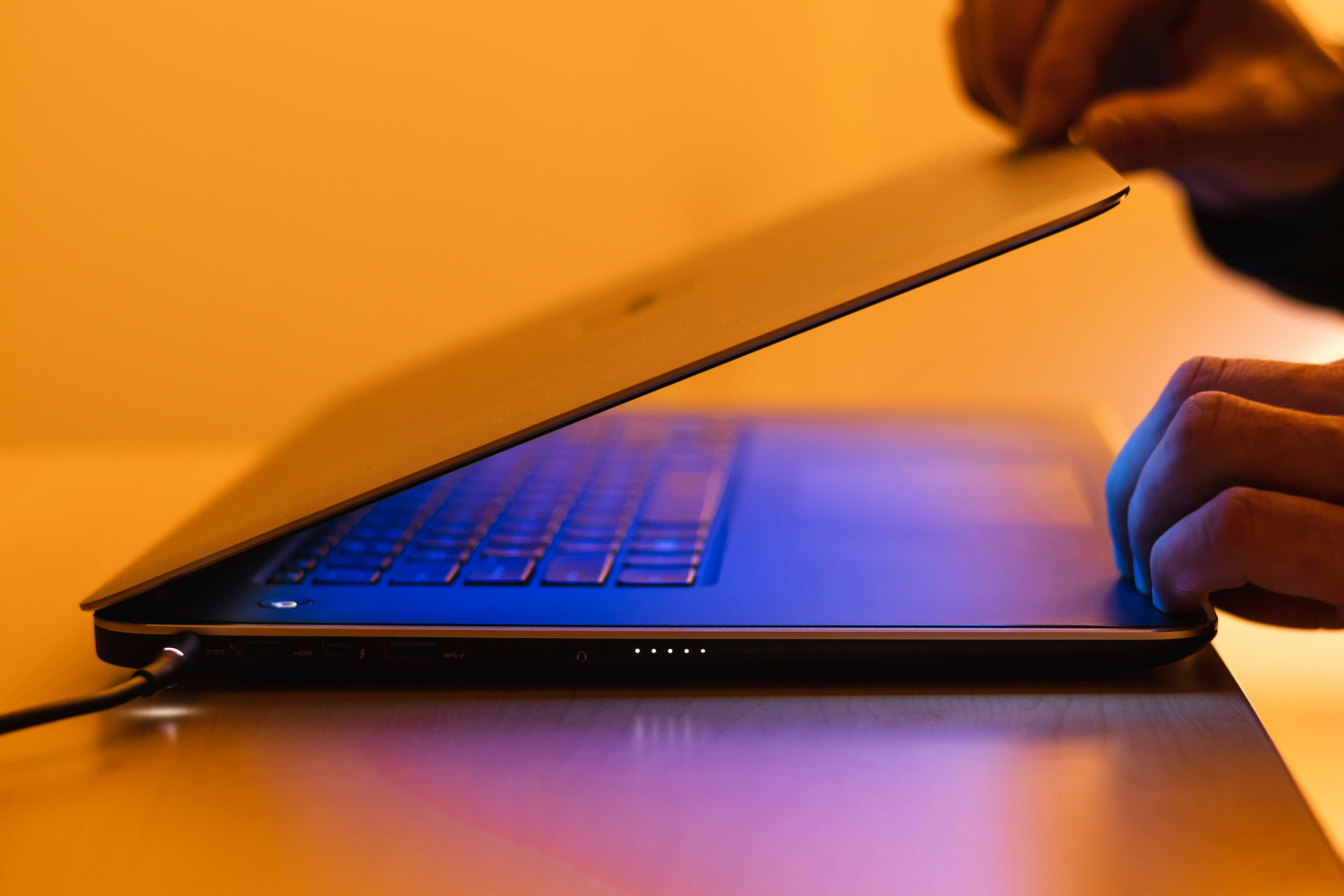 Halb geöffneter Laptop in orange-blauer Beleuchtung, rechts liegt eine Hand auf dem Gerät.