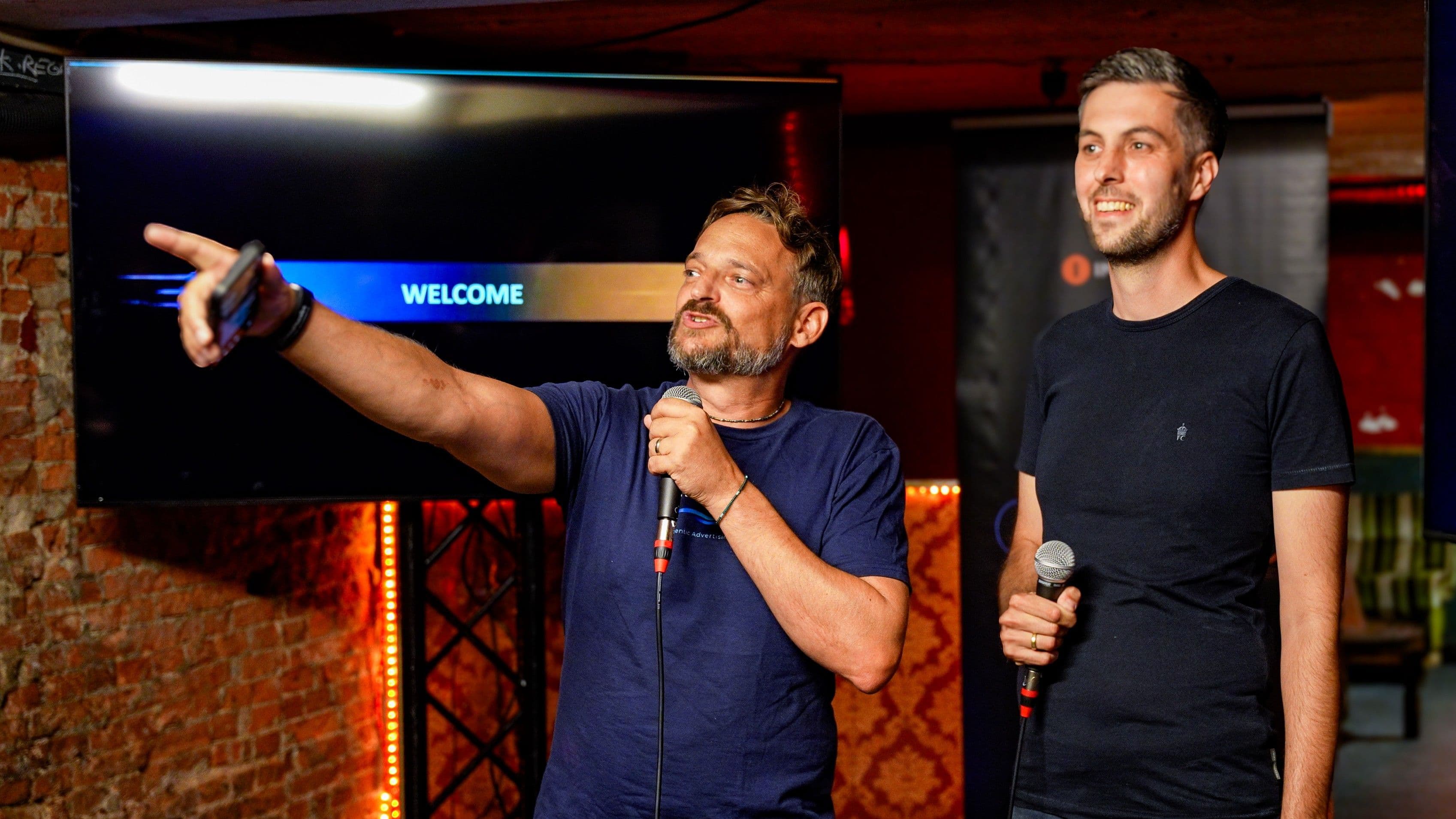 Jörg Schneider und David Porzelt beim Agentic Advertising Kickoff in Hamburg mit Mikrofonen vor einem Veranstaltungsbildschirm.