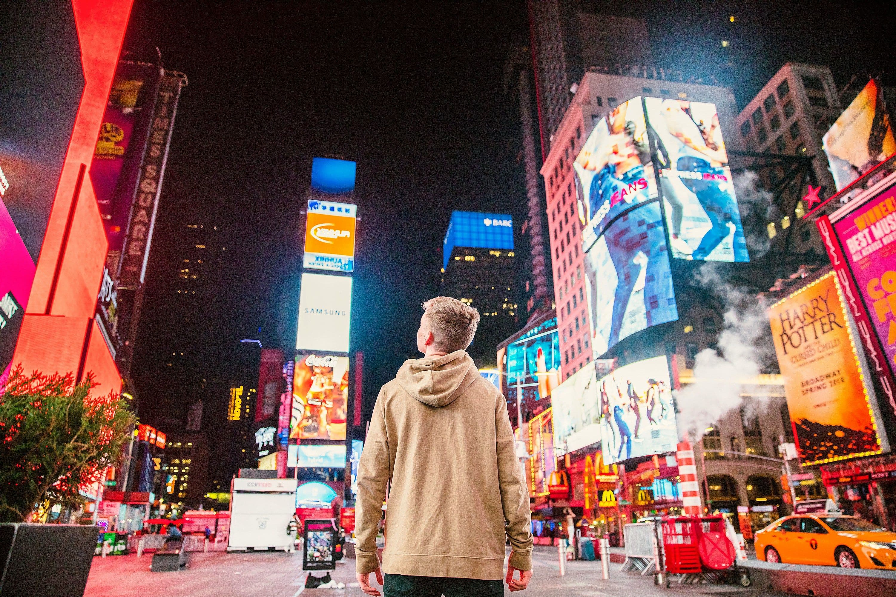 Ein junger Mann vor glitzernder Außenwerbung in einer urbanen. nächtlchen Umgebung.