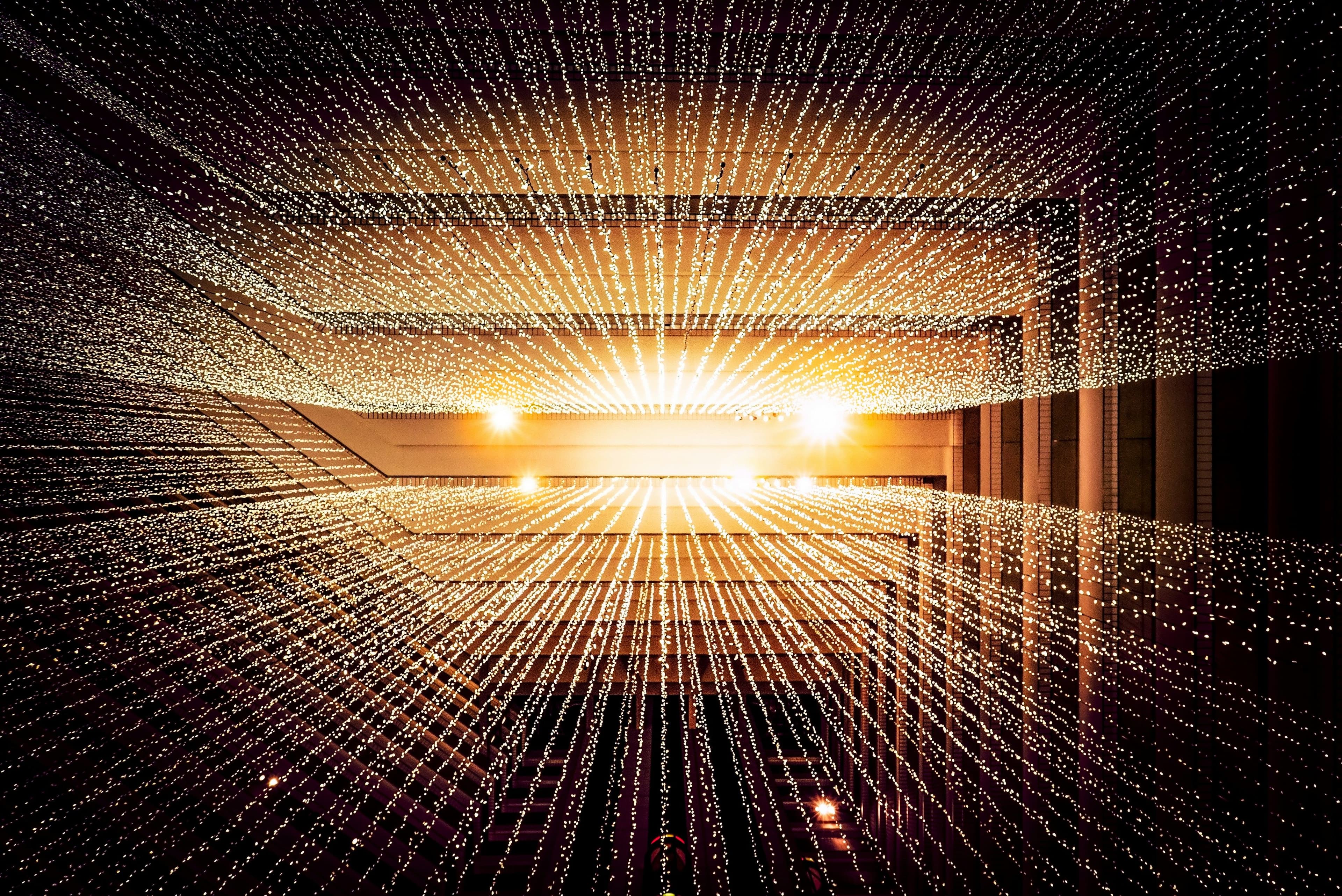 Dichtes Netz aus warm leuchtenden Lichtpunkten und Linien in einer großen Innenrauminstallation.