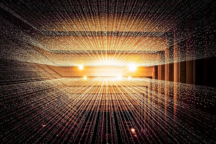 Dichtes Netz aus warm leuchtenden Lichtpunkten und Linien in einer großen Innenrauminstallation.