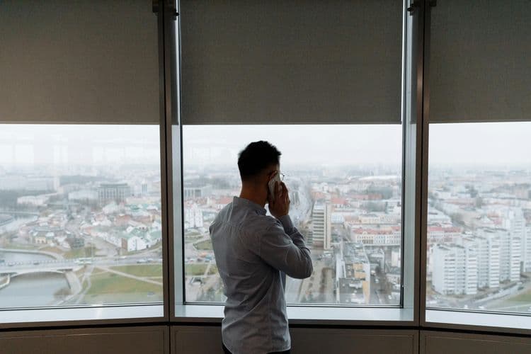 Ein Mann telefoniert vor einer großen Fensterfront mit Blick über eine Stadt.