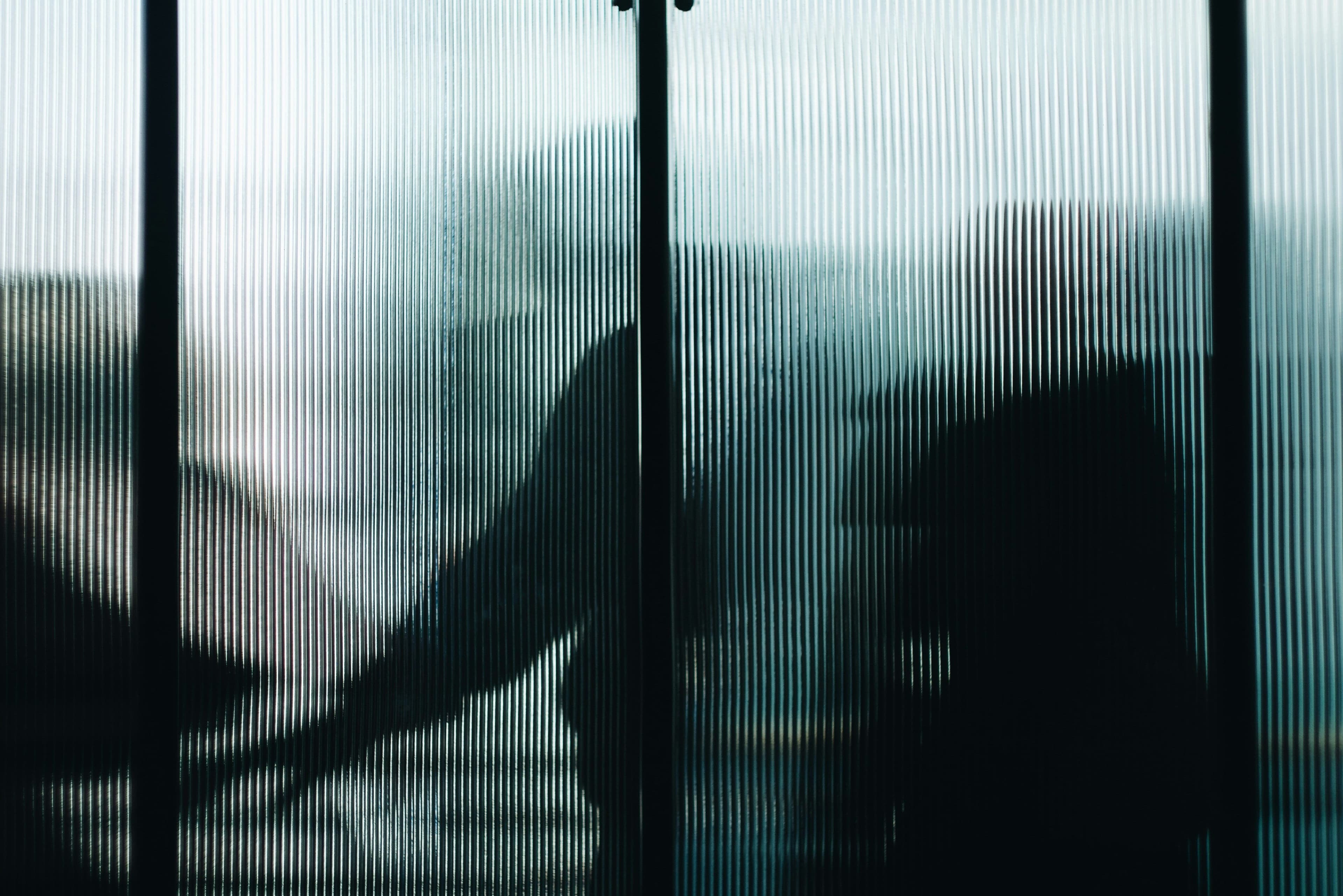 Verschwommene Silhouetten von Menschen hinter einer geriffelten Glasfläche.