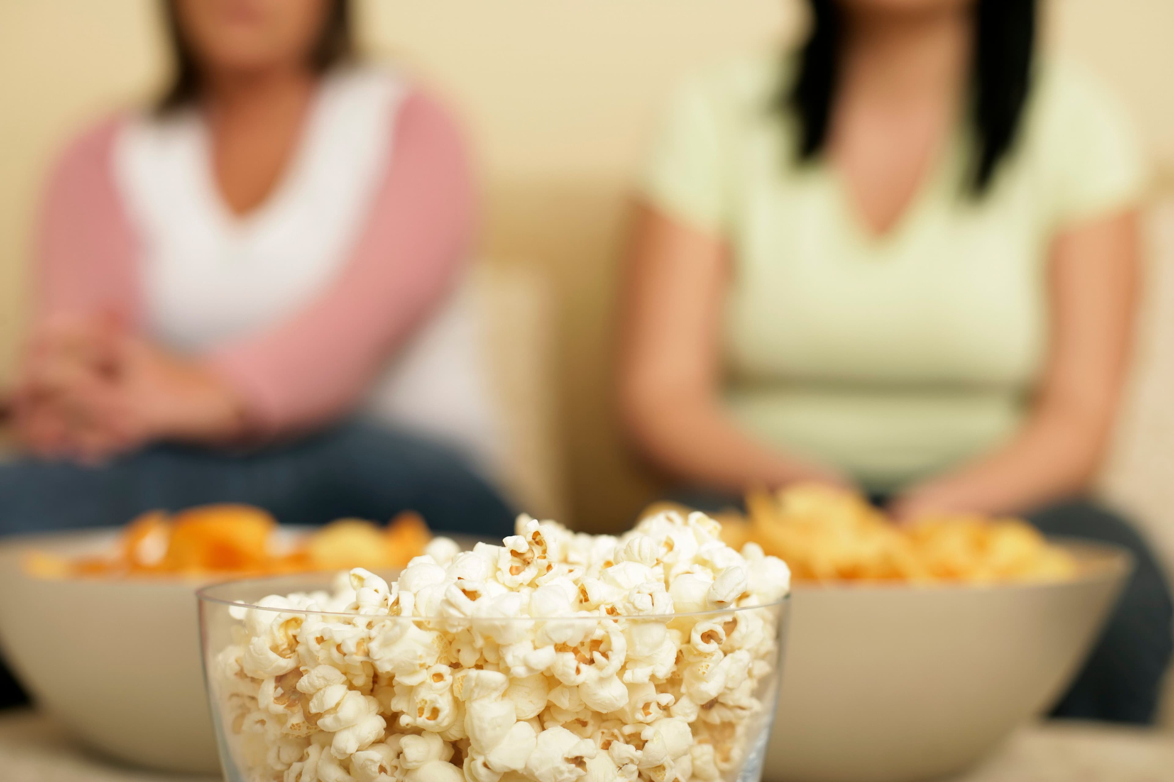 Schale mit Popcorn im Vordergrund, dahinter sitzen zwei Personen unscharf auf einem Sofa.