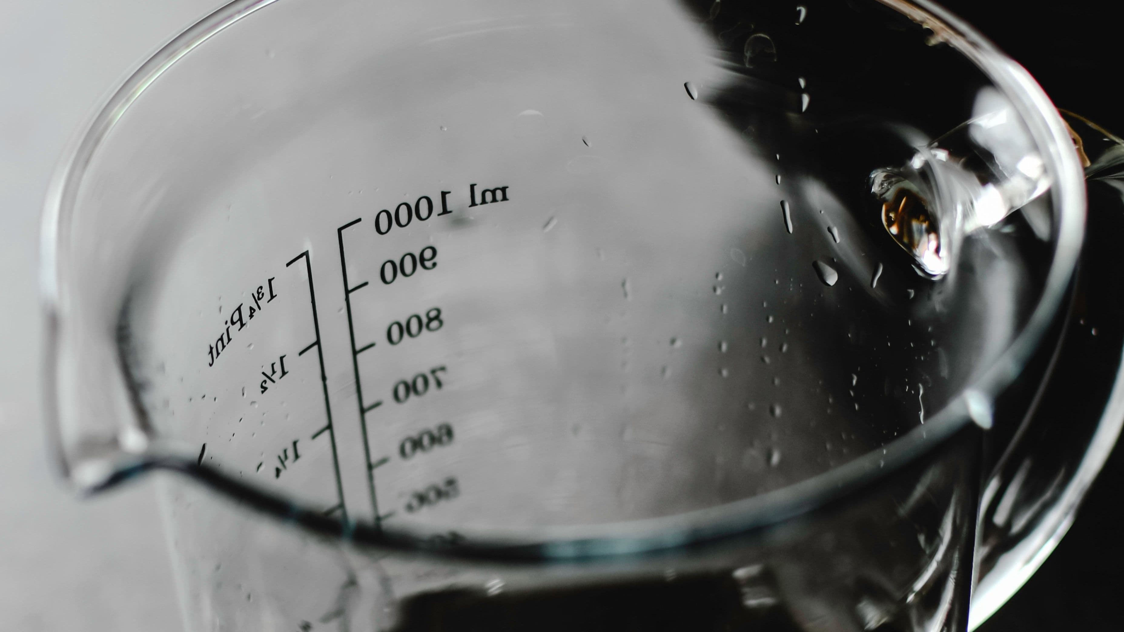 Messbecher aus Glas mit gut sichtbarer Skala vor dunklem Hintergrund.