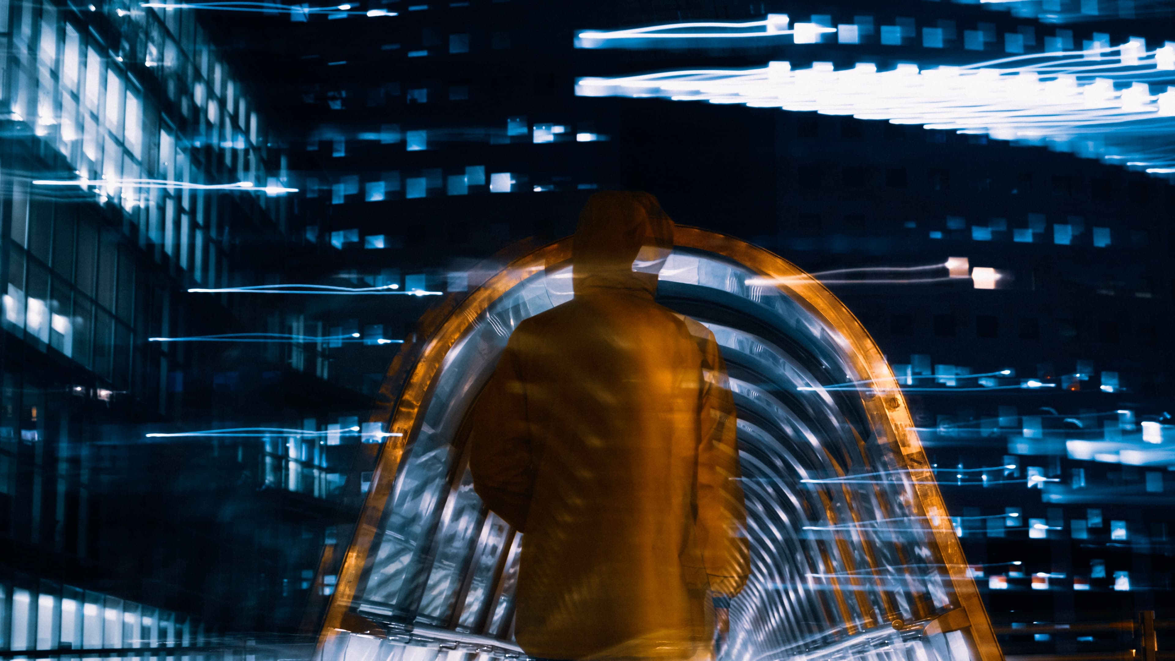 Unscharfe Person in einer beleuchteten, futuristisch wirkenden Passage mit blauen und orangefarbenen Lichtspuren.