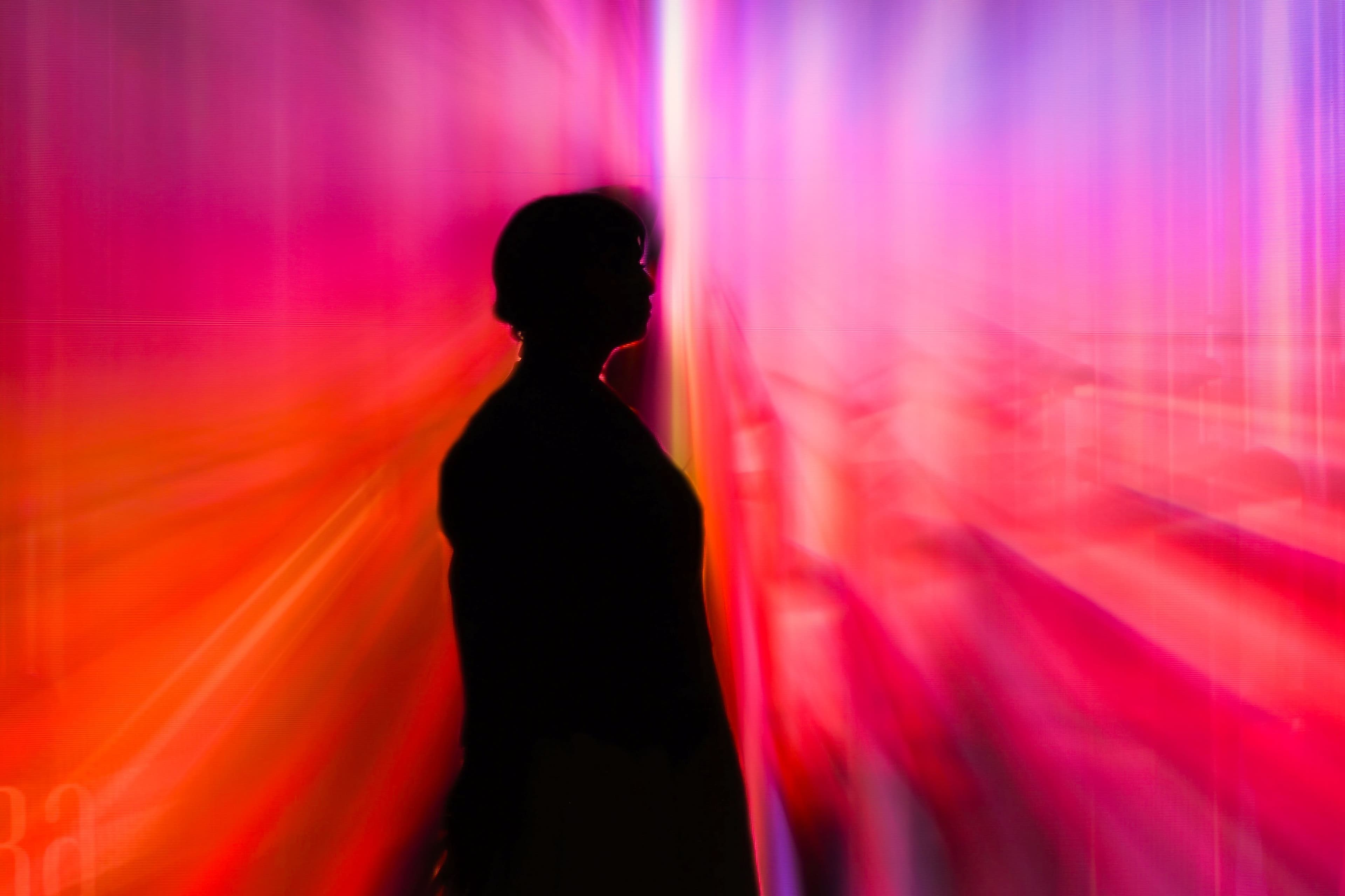 Silhouette einer Person vor einer leuchtenden Installation in Rot-, Pink- und Violetttönen.