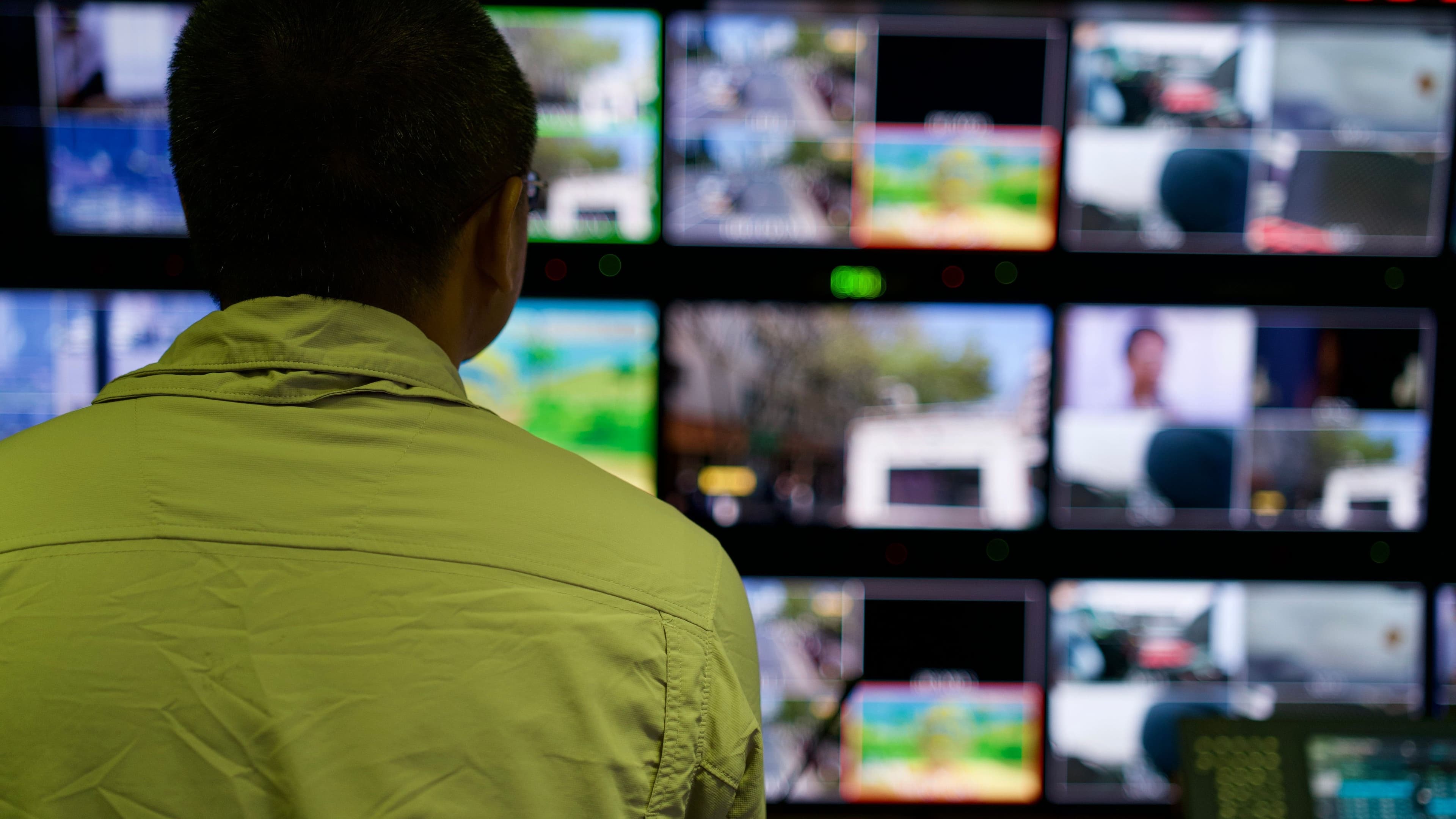 Person vor einer Monitorwand in einem Fernseh-Kontrollraum.