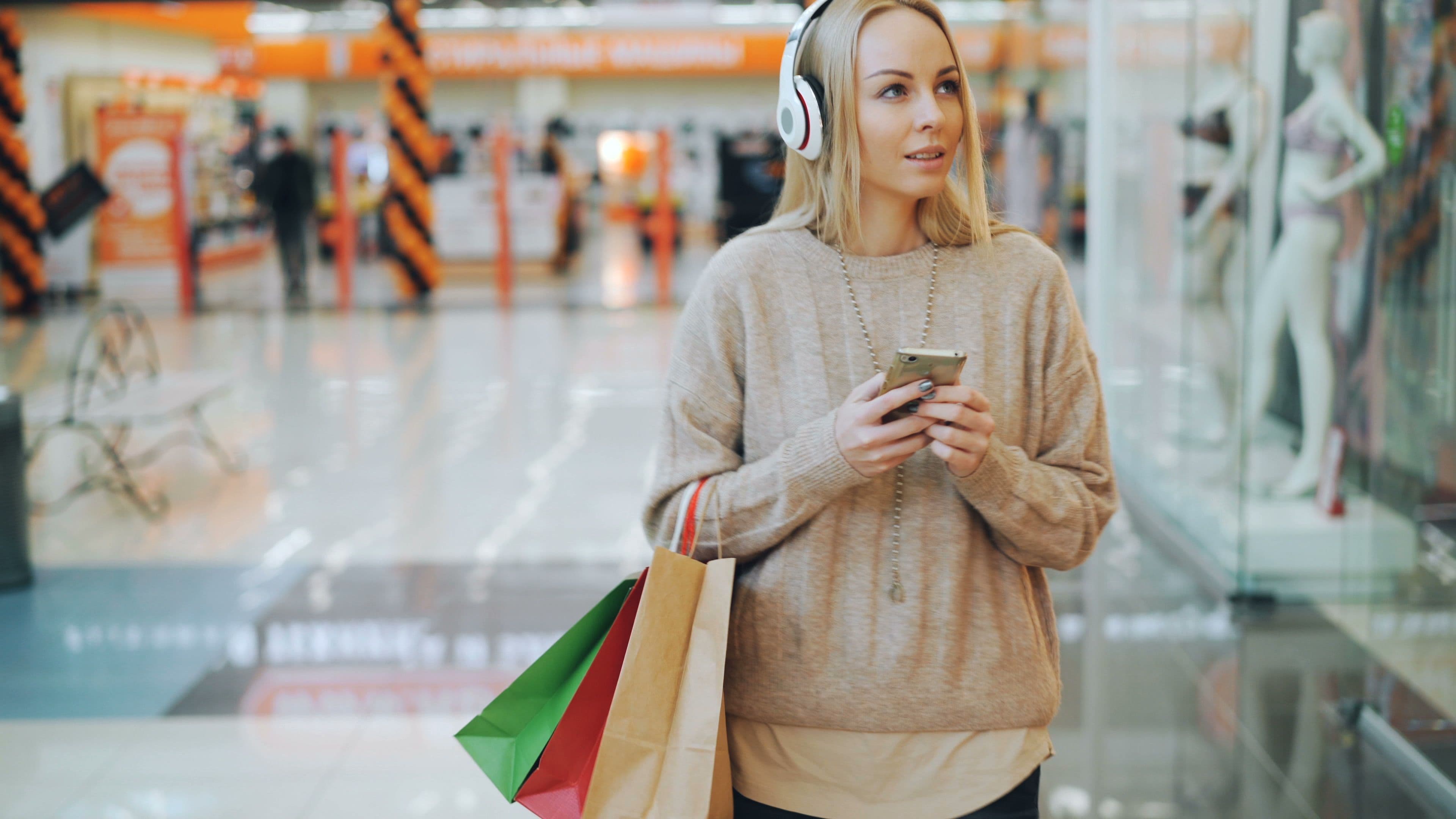 Frau mit Smartphone und Einkaufstaschen in einem Einkaufszentrum.