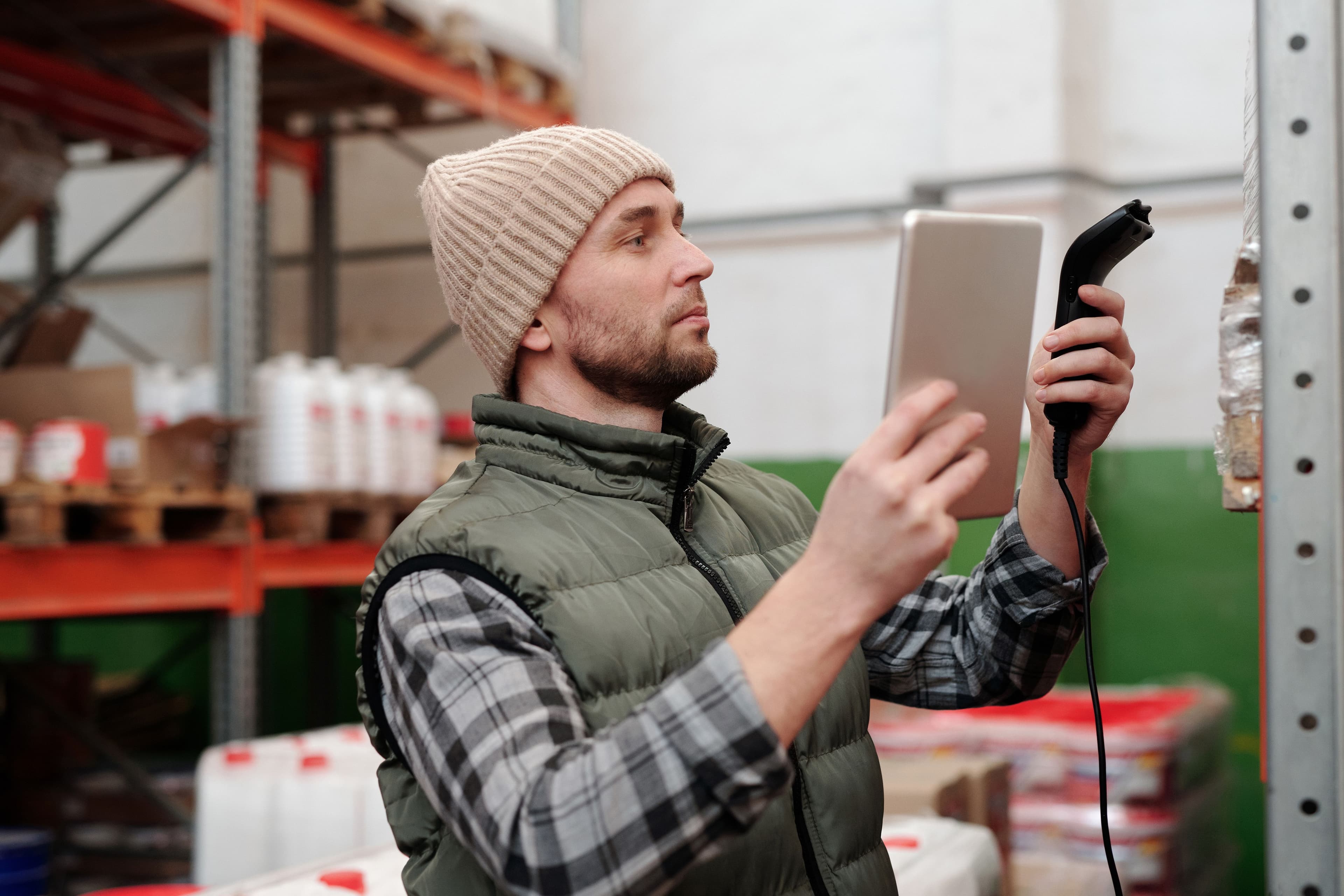 Mitarbeiter in einem Lager arbeitet mit Tablet und Handscanner an einem Regal.