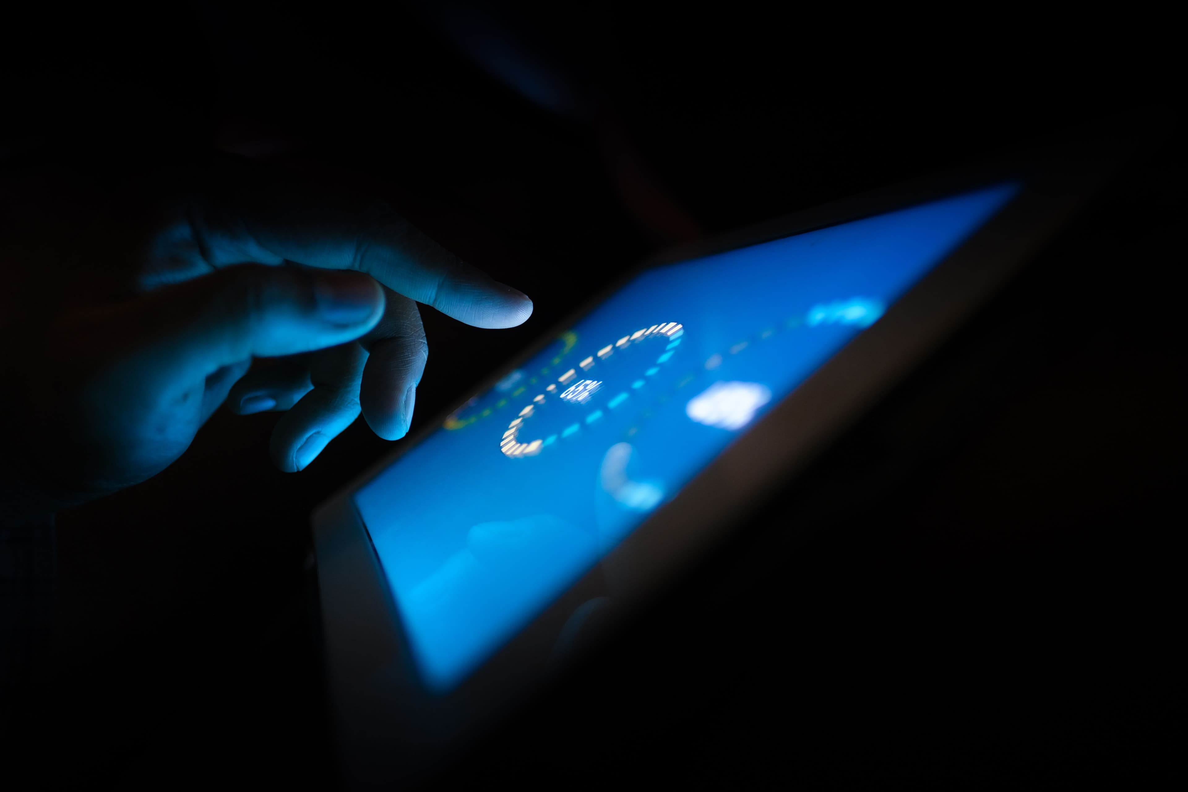 Eine Hand bedient in dunkler Umgebung eine leuchtende digitale Oberfläche.